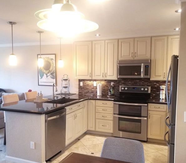 Modern kitchen with cream cabinets, black countertops, stainless appliances, and hanging pendant lights