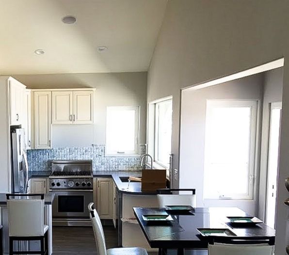 Bright kitchen and dining area with white cabinets, blue backsplash, and a table by large windows