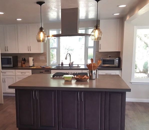 Modern kitchen with dark island, white cabinets, pendant lights, and a window above the sink.