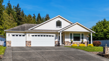 Suburban house with a two-car garage, front porch, and landscaped yard under a clear blue sky