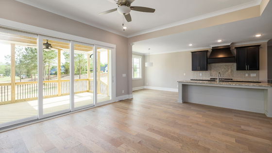 Empty open-plan living room and kitchen with hardwood floors, sliding glass doors, and ceiling fan.