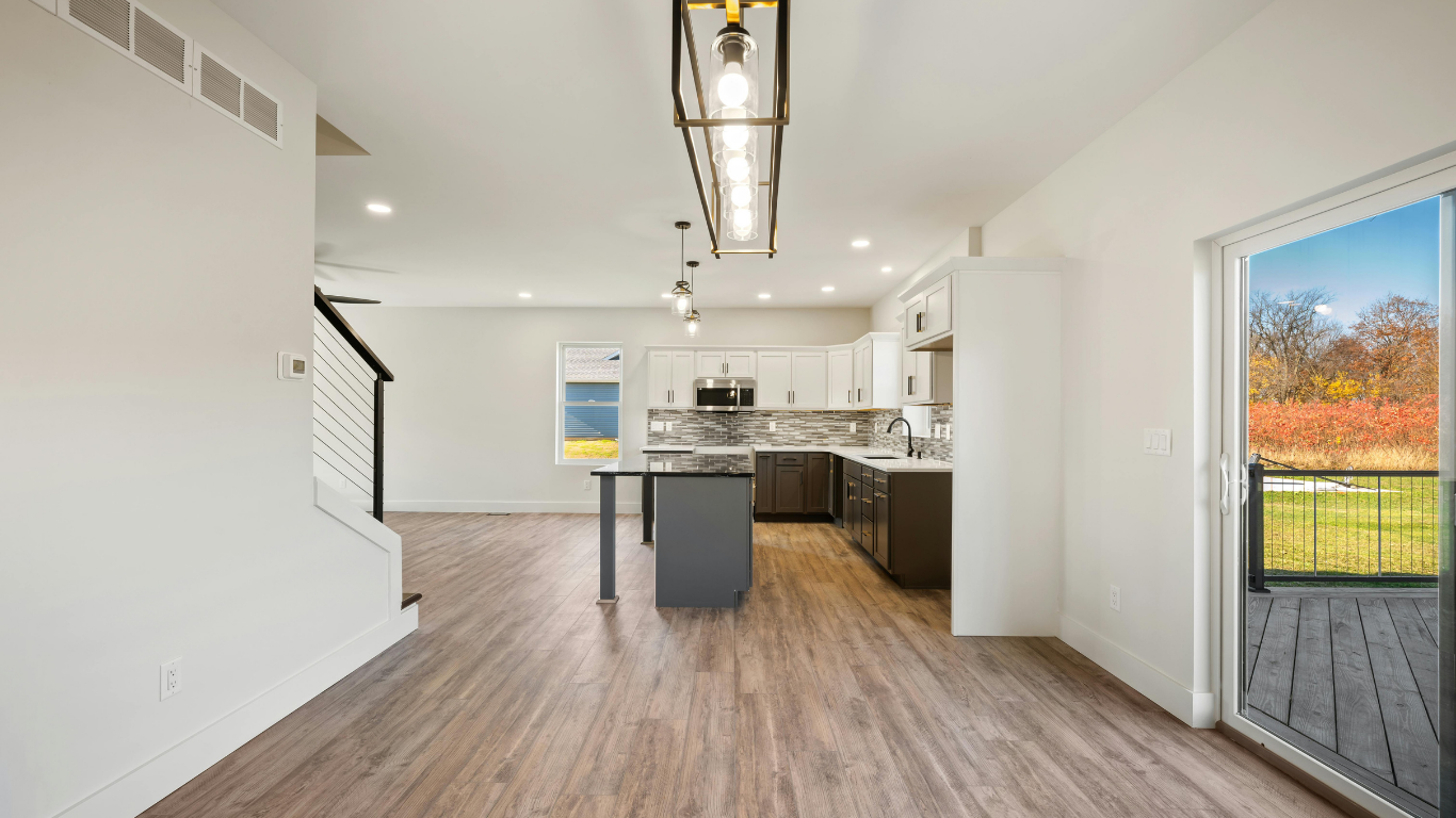 Bright open-plan kitchen and living area with white walls, wood floors, island, and sliding door to deck