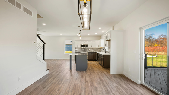Bright open-plan kitchen and living area with white walls, wood floors, island, and sliding door to deck