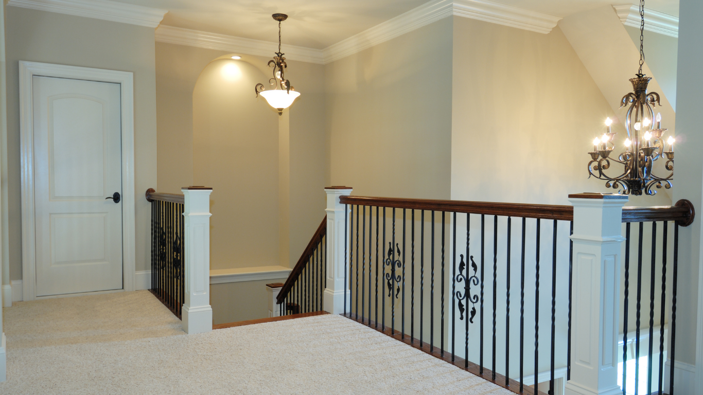 Bright upstairs landing with beige walls, carpet, hanging light, and black iron stair railing.