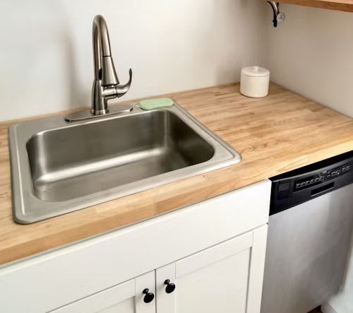Stainless steel sink in kitchen with wood countertop, white cabinets, and dishwasher.