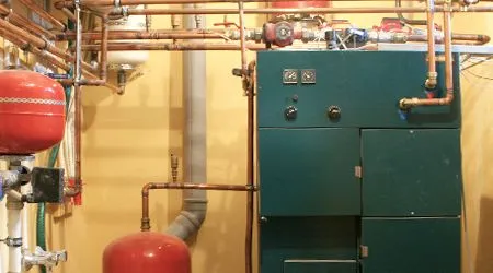 A boiler with copper pipes and red tanks in a utility room.