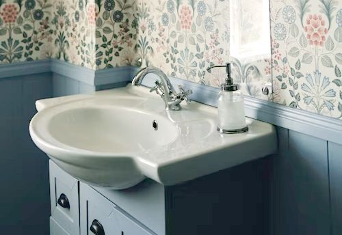 White sink with chrome faucet and soap dispenser, blue paneling, floral wallpaper.