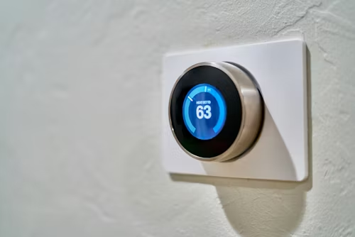 Smart thermostat displaying 63 degrees on a white wall.