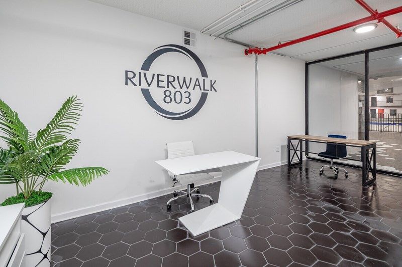 Riverwalk803 entrance, with a sign of the logo on a wall and desks below
