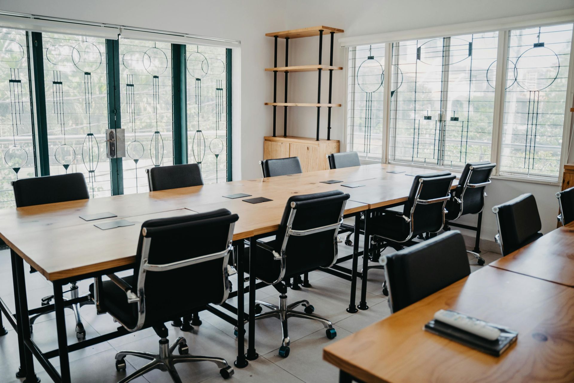 Conference room with a large wooden table, black chairs, and windows.