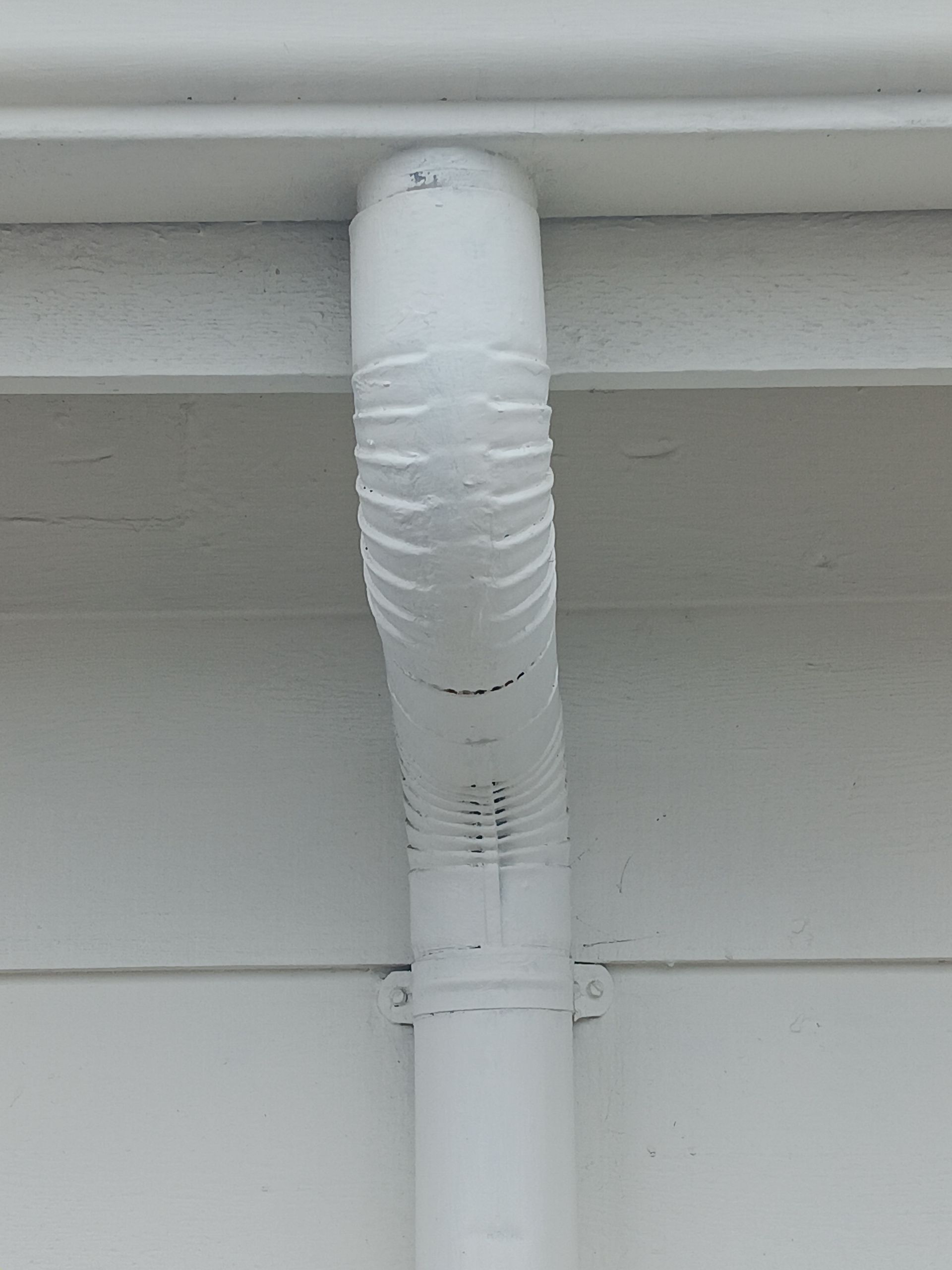 Worker installing a copper downspout on a house exterior while kneeling by the wall