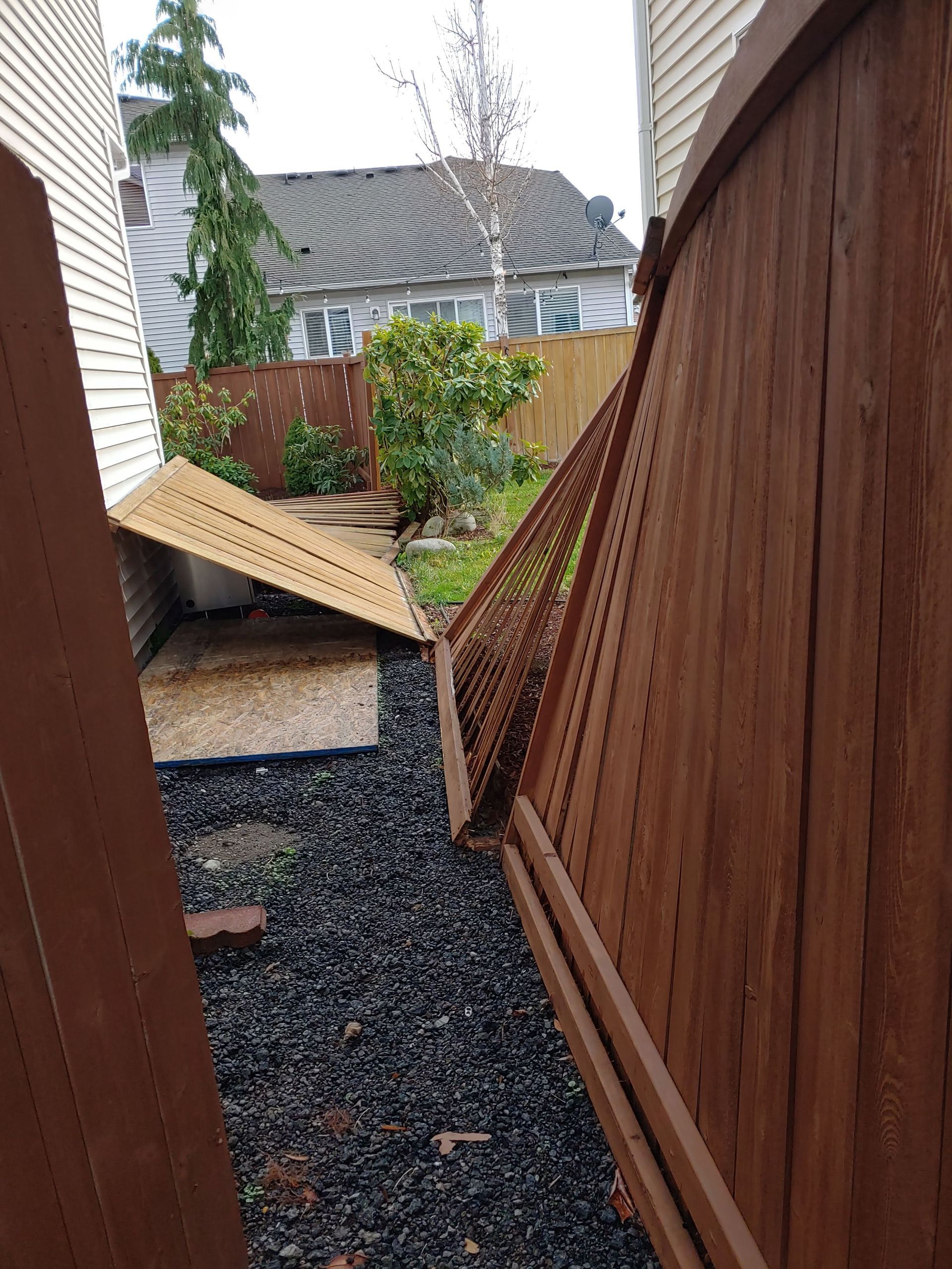 A wooden fence is broken in half in a backyard.
