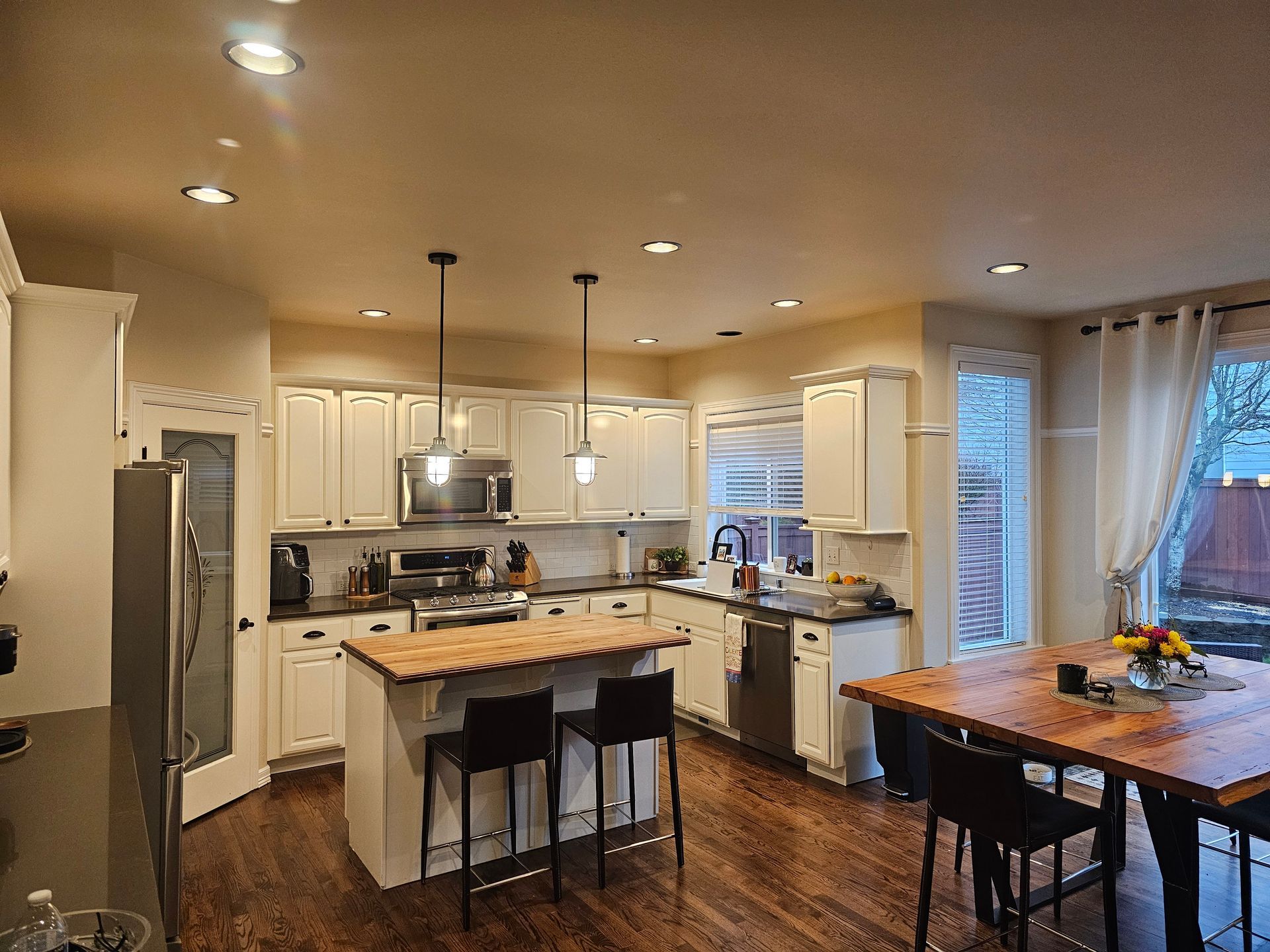 A kitchen with white cabinets , stainless steel appliances , a wooden table and chairs.
