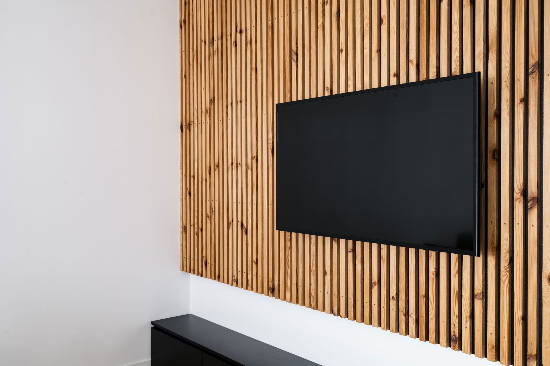 A wall-mounted black television screen centered on a wall covered in vertical wooden slats above a black cabinet.