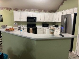 Kitchen with white cabinets, green island, black appliances, and stainless steel refrigerator under floral wallpaper border