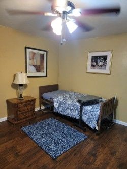 Small bedroom with a single bed, blue rug, nightstand, lamp, and ceiling fan.