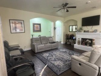 Living room with gray seating, patterned rug, wall-mounted TV, and fireplace mantel