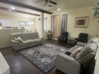 Living room with gray sofas, patterned rug, and chairs near a window and kitchen pass-through