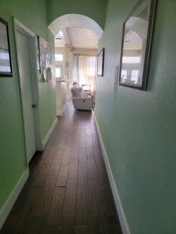 Narrow green hallway leading to a bright room with a white chair and arched ceiling.