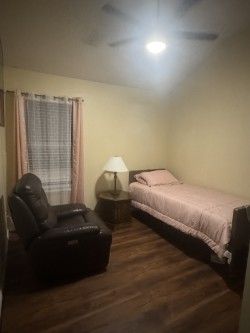 Small bedroom with a twin bed, black recliner, nightstand lamp, window, and wood floor.