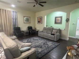 Living room with beige sofas, dark chairs, patterned rug, and green accent walls under a ceiling fan