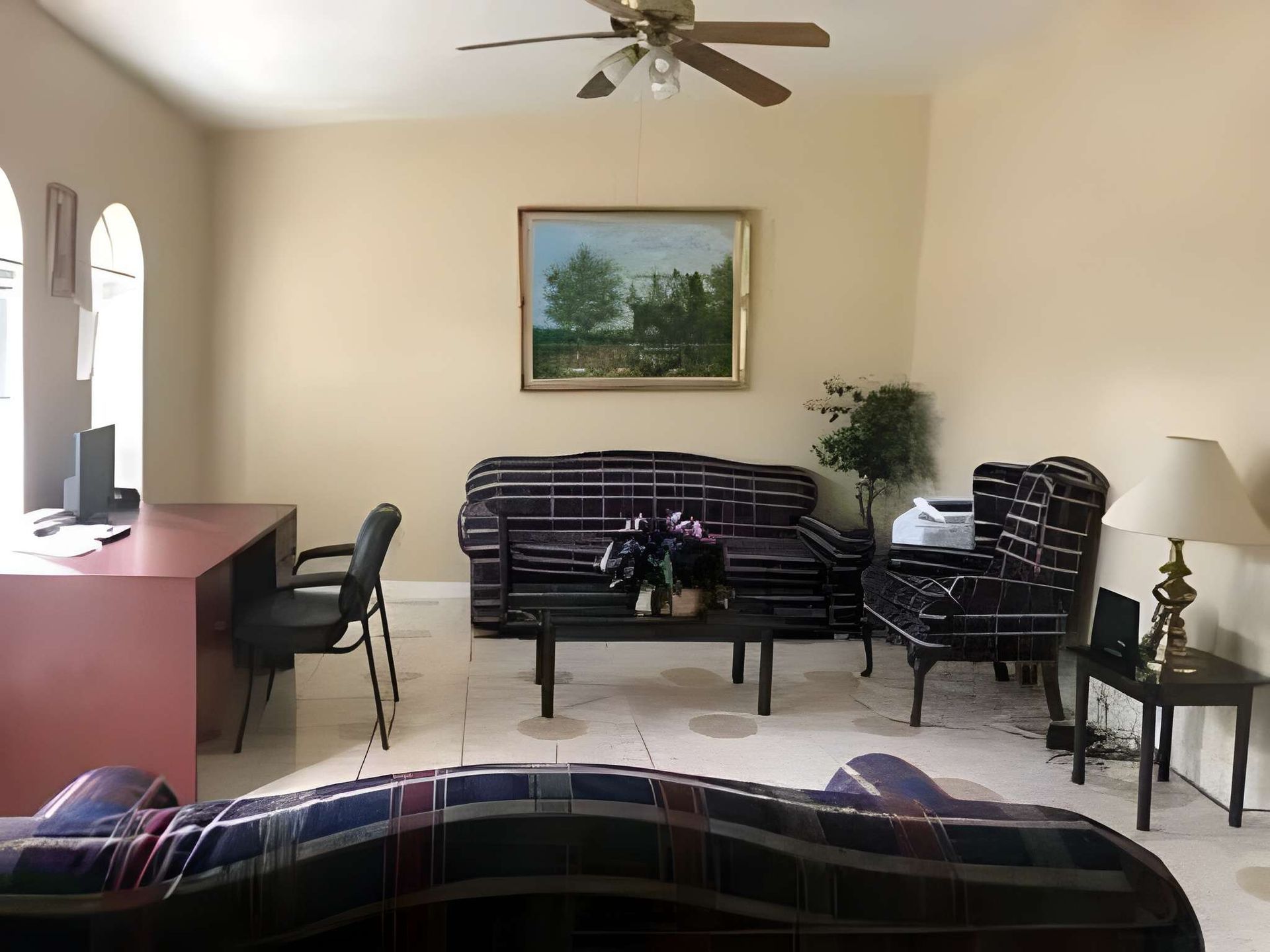 Living room with plaid sofas, table, desk, lamp, and wall painting under a ceiling fan.