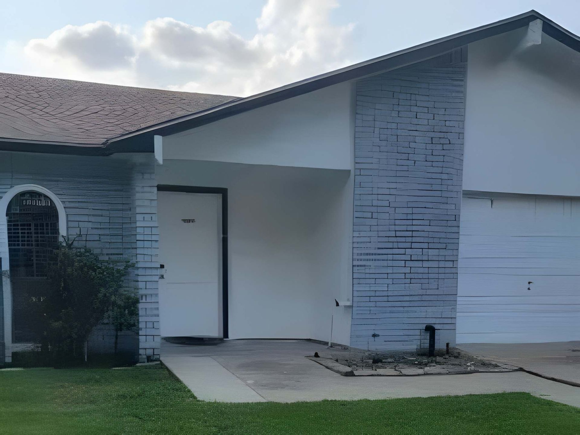 Front entrance of a house with white brick walls, a garage, and a small front walkway