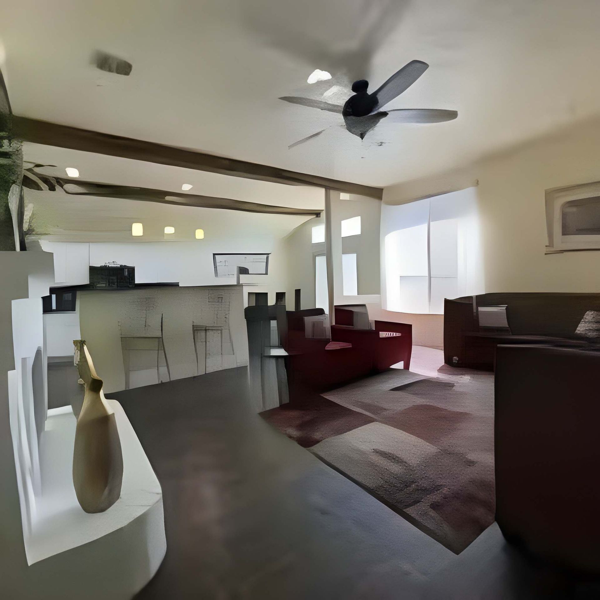 Open living room with kitchen, red chairs, rug, ceiling fan, and sunlight from a large window