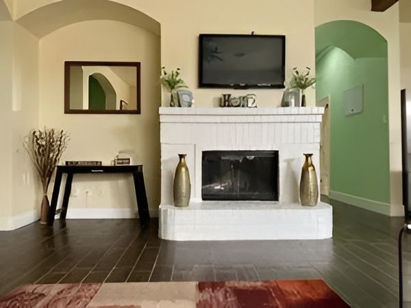 Living room with white fireplace, wall-mounted TV, green accent wall, and dark hardwood floors