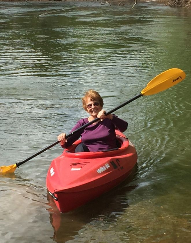 A woman is paddling a red kayak on a river.