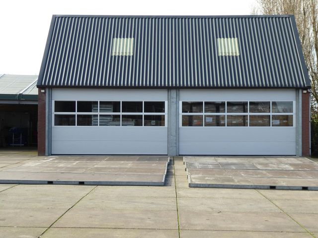 Gray garage with two bays, corrugated roof, small windows, and concrete slabs in front.