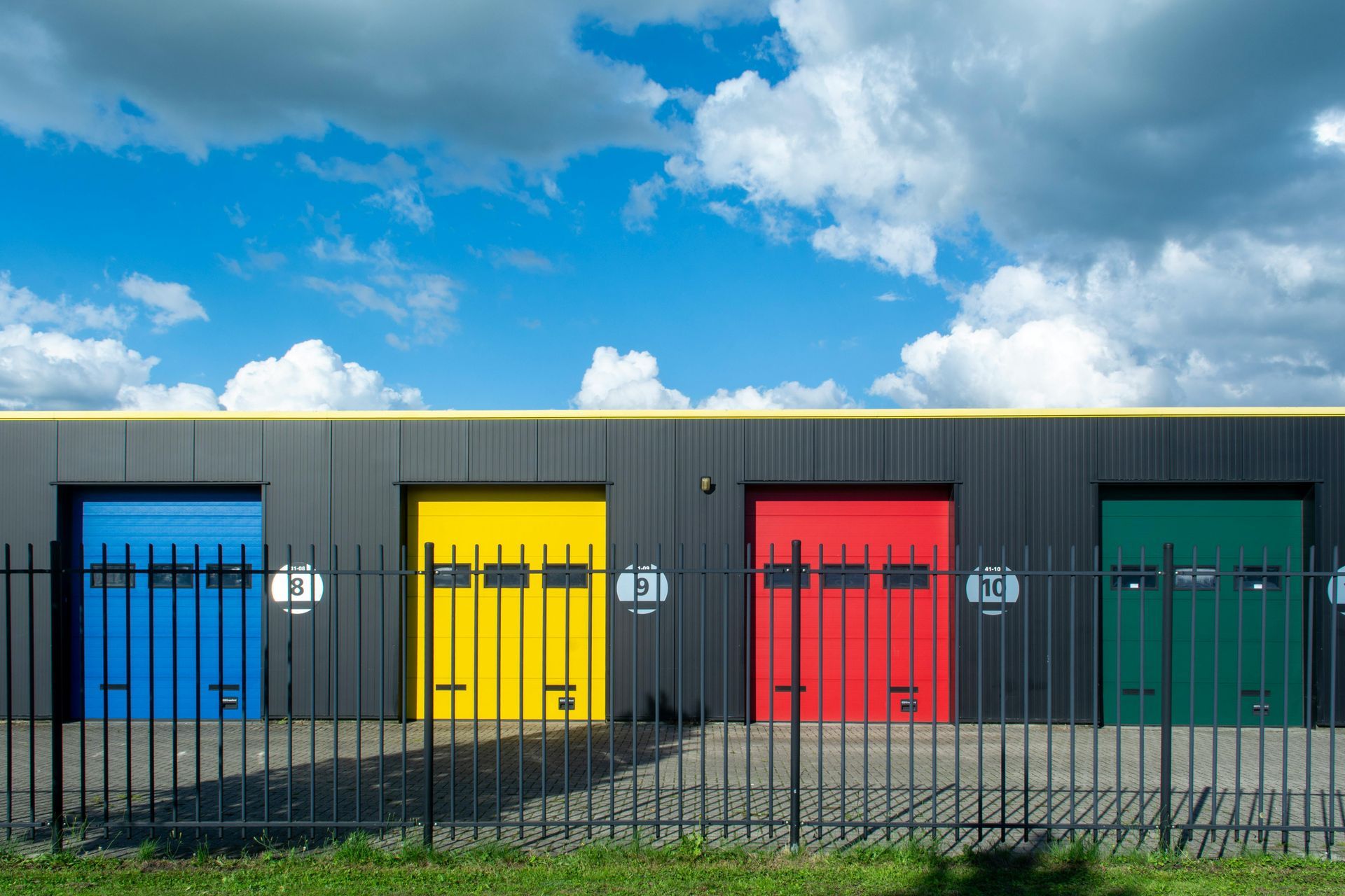 Row of storage units with blue, yellow, red, and green doors behind a black fence.