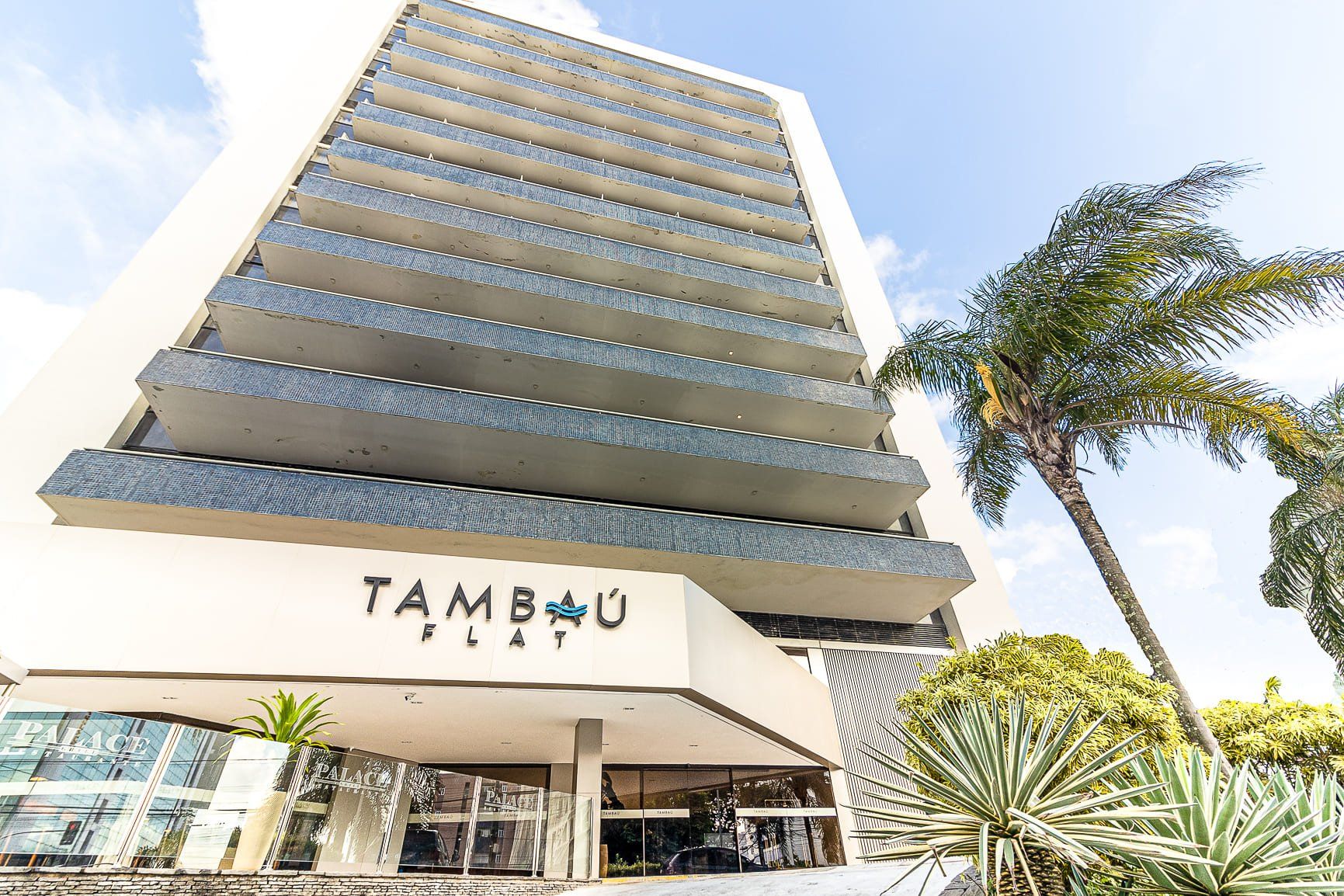 Entrada de hotel de vários andares com palmeiras e o nome “TAMBAU” na fachada.
