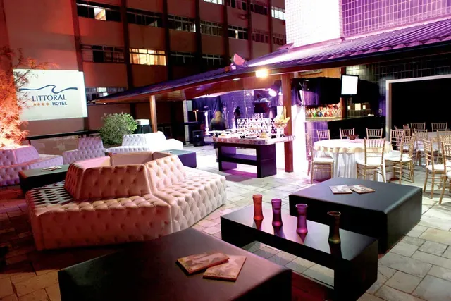Elegante lounge na cobertura com assentos almofadados, mesas baixas e vista para as luzes da cidade à noite.