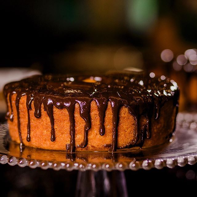 Bolo Bundt com cobertura de chocolate, em um suporte, iluminado suavemente contra um fundo escuro.