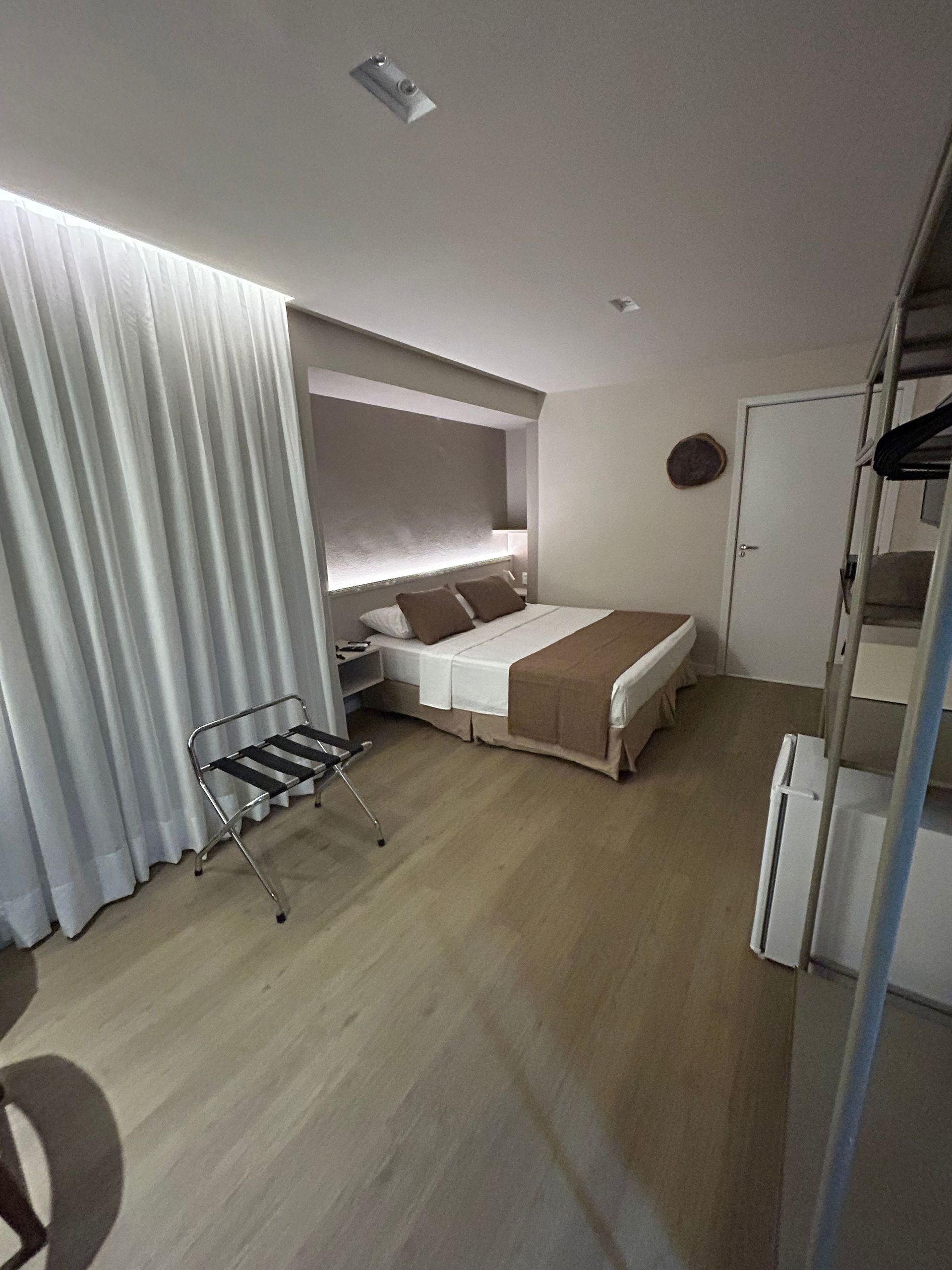 Quarto moderno com cama, cortinas, piso de madeira e closet aberto.