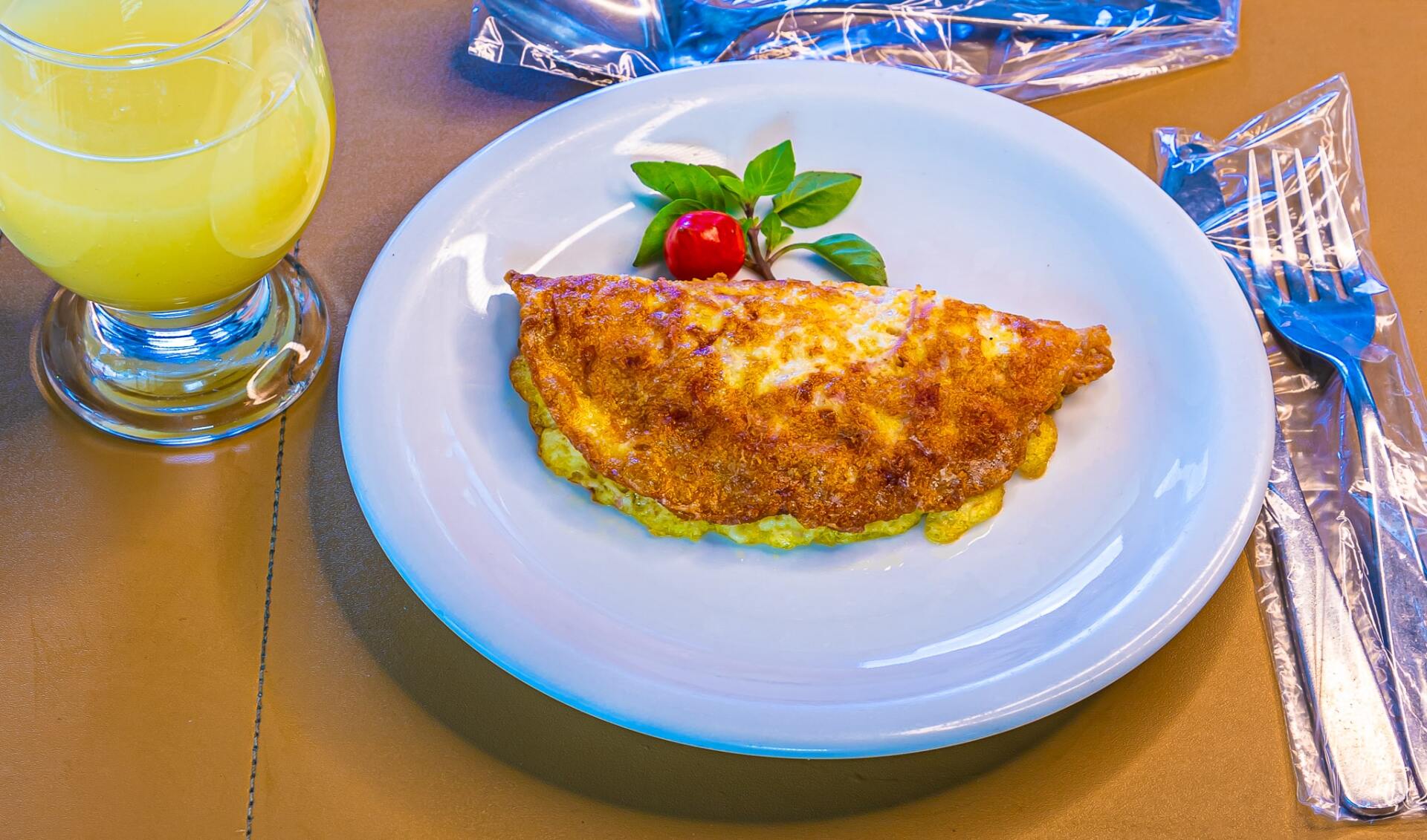 Omelete em um prato branco com tomates, servida ao lado de um copo de suco de laranja e talheres sobre a mesa.