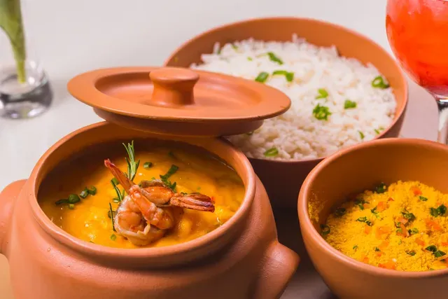 Panelas de barro com curry, arroz e legumes temperados servidas em uma mesa.