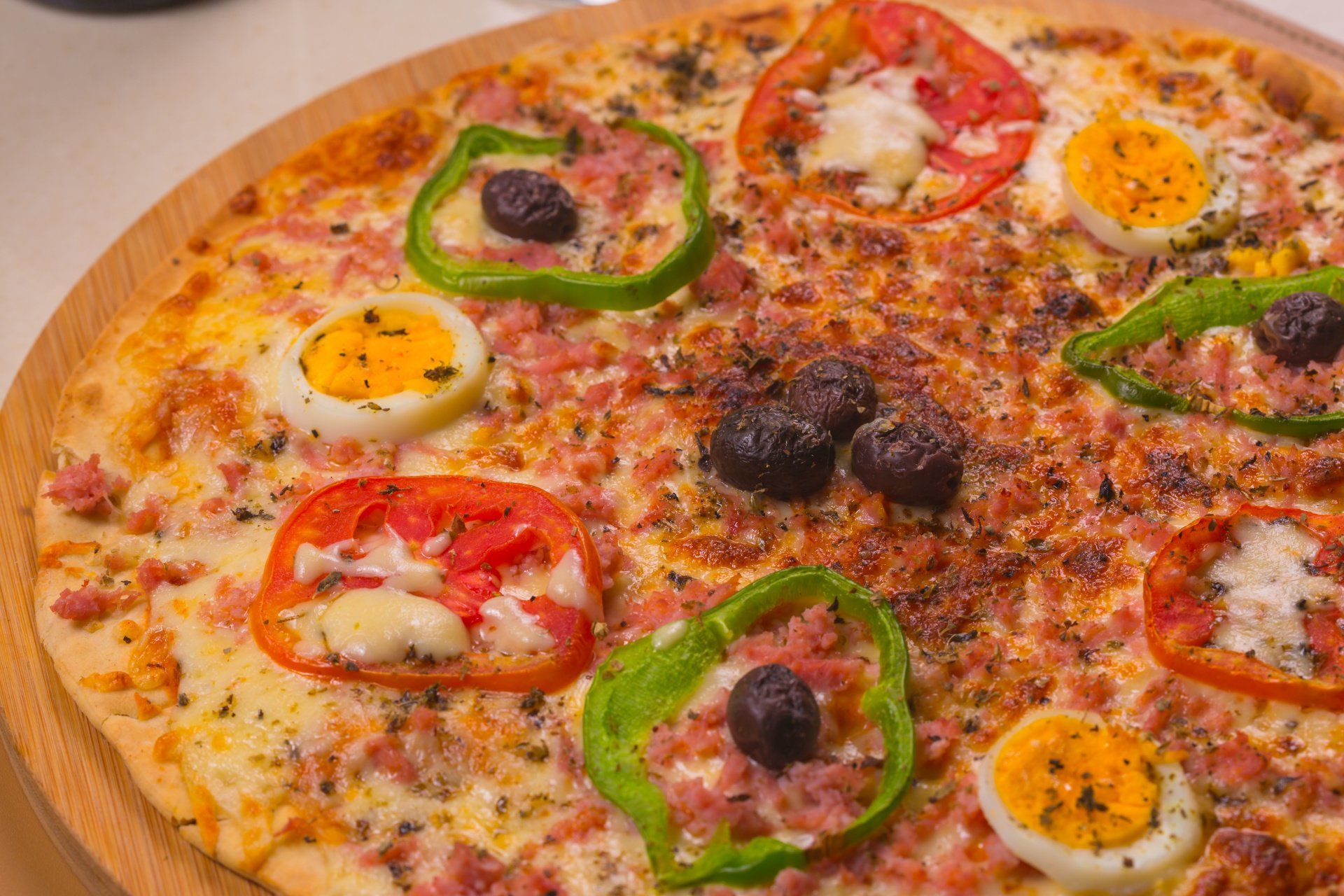 Pizza coberta com rodelas coloridas de pimentão, azeitonas e queijo derretido, servida em uma tábua de madeira.