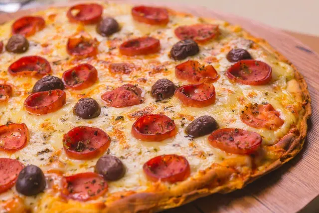 Pizza de pepperoni e azeitonas em uma tábua de madeira