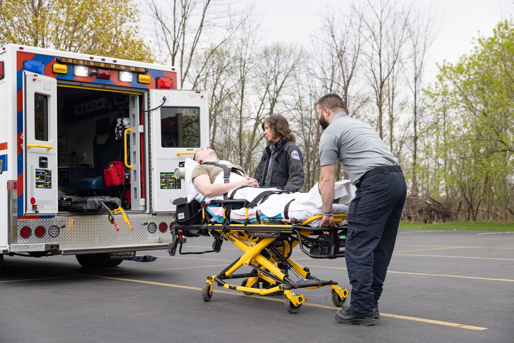 Paramedics load a simulated patient on a stretcher into an ambulance