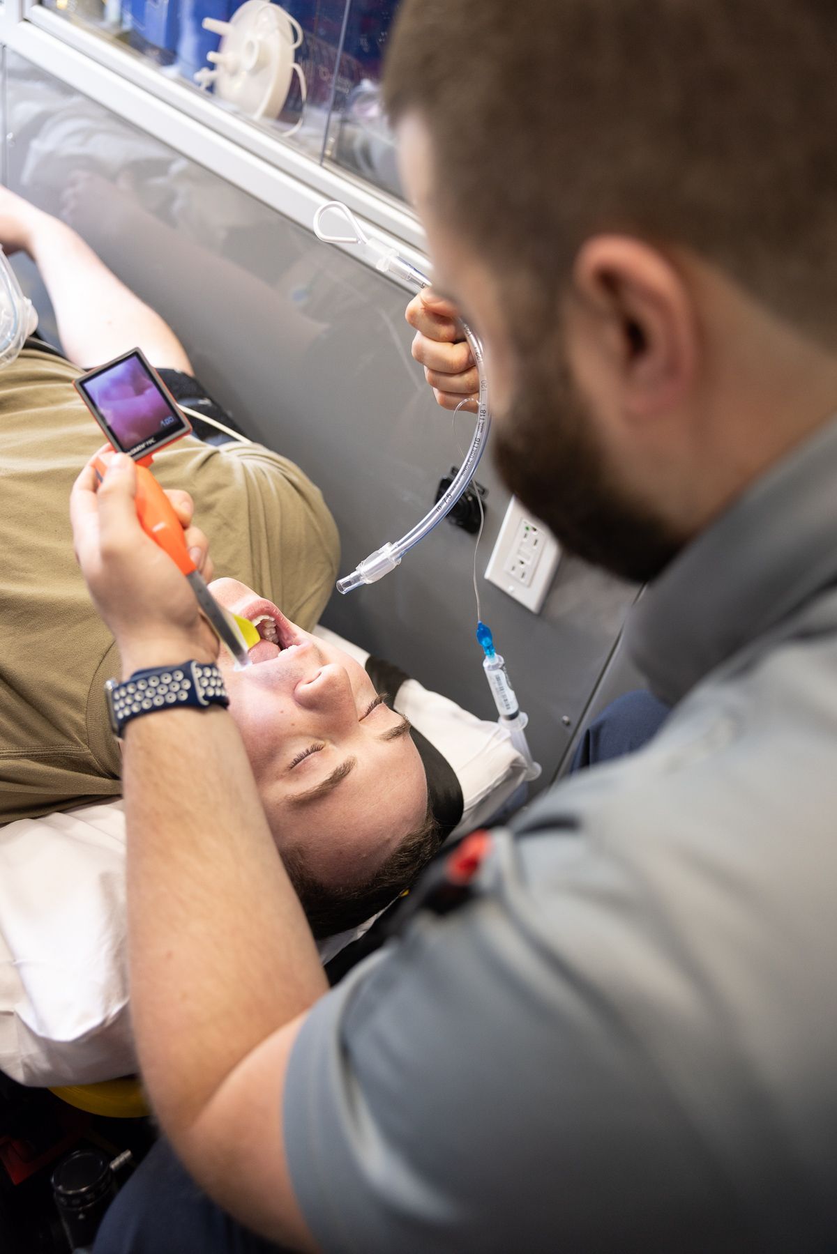 Paramedic treating a patient on a stretcher, using a mask and monitoring equipment in an ambulance