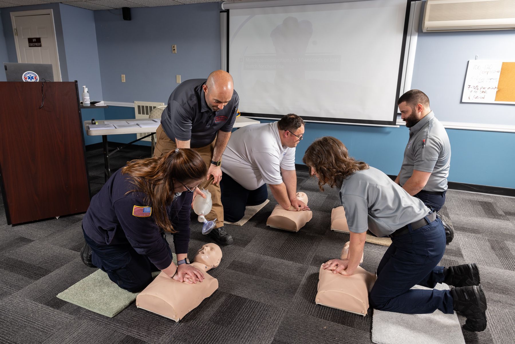 People practicing CPR on mannequins in a classroom with an instructor supervising
