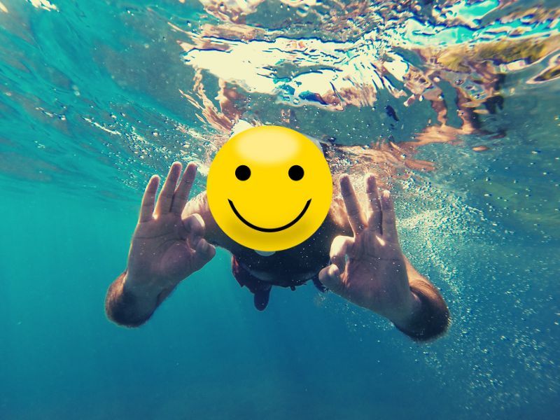 Person with smiley face mask underwater, making 