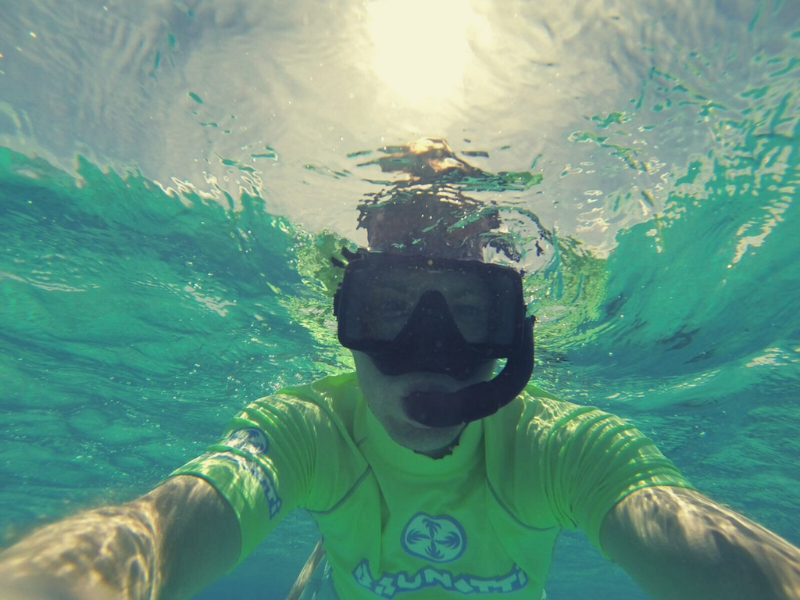 Person snorkeling in clear turquoise water, sun overhead.