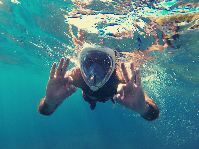 Person snorkeling underwater with a full-face mask, giving the 