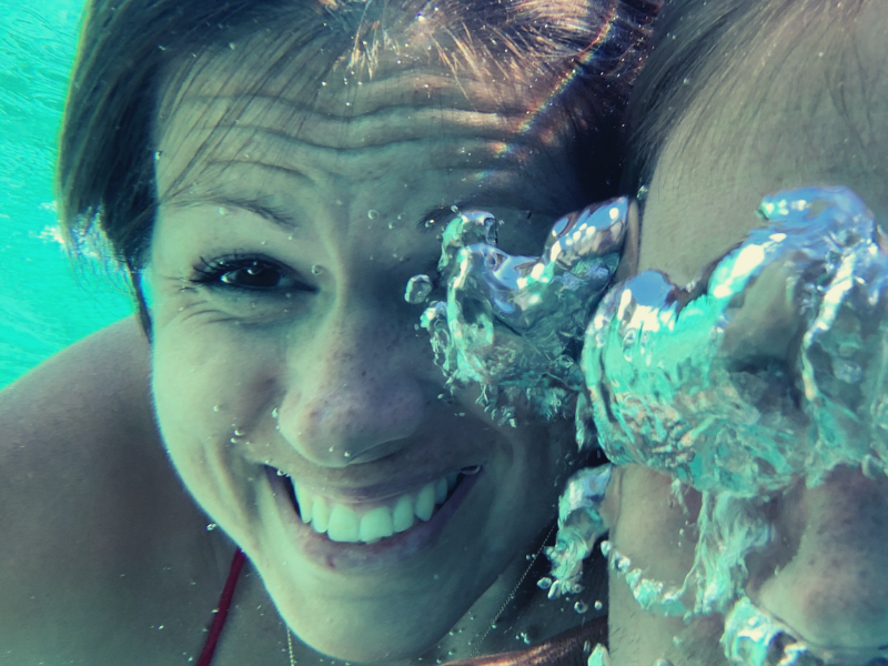 Woman smiling underwater with bubbles.