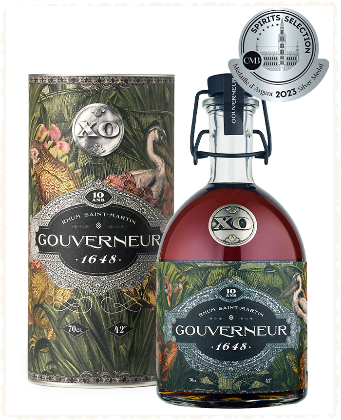 Bottle of XO Gouveneur 1648 rum with elaborate label, tropical design, next to its tube packaging. Award seal at top.