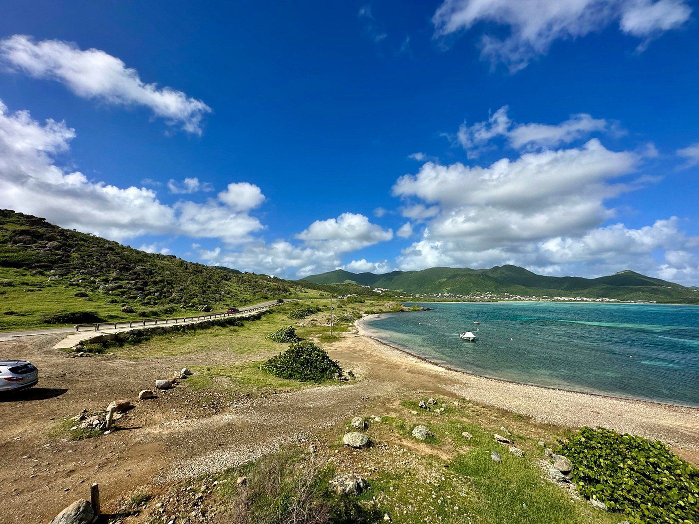 Beachside landscape with blue sky, green hills, and turquoise water.