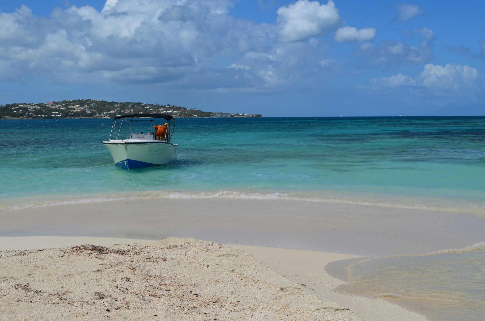 Boat in turquoise water near a sandy beach under a blue sky.